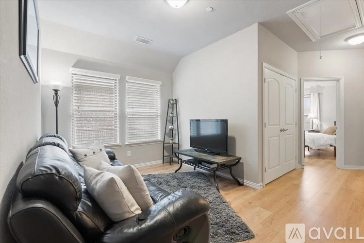 A black leather couch sits in a living room with a television and a black and white rug.