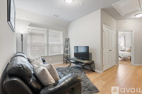 A black leather couch sits in a living room with a television and a black and white rug.