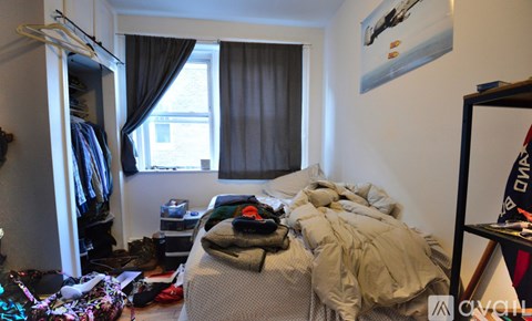 A messy bedroom with a bed covered in blankets and clothes.