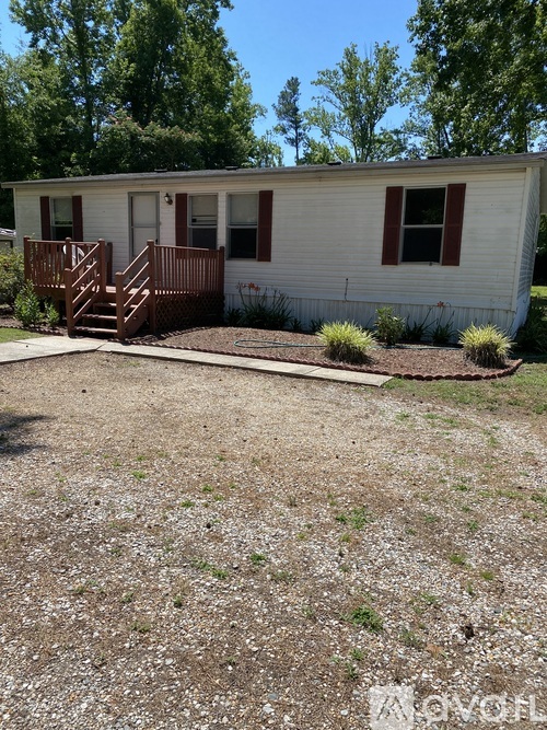 A small white house with a brown deck in the front yard.