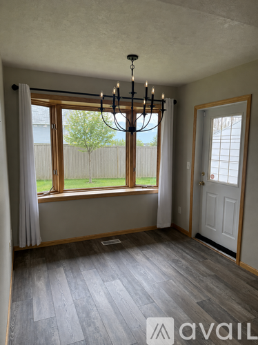 A room with a chandelier and a window with a view of a fence and trees.