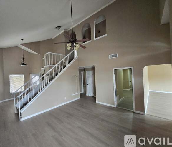 A spacious living room with a staircase and a ceiling fan.
