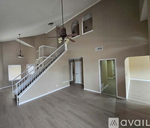 A spacious living room with a staircase and a ceiling fan.
