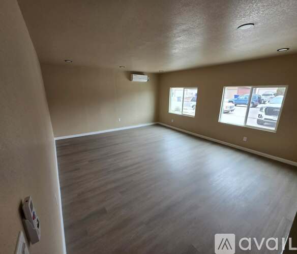 A spacious room with wooden flooring and a window overlooking a parking lot.