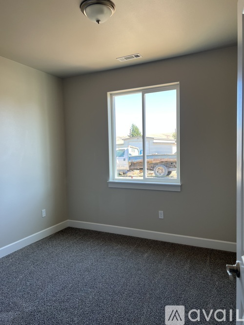 A room with a carpeted floor and a window showing a view of a house and trees.