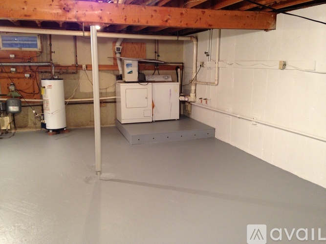 A room with a white floor and a white wall with pipes and a water heater.