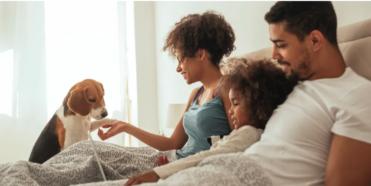A family of three is sitting on a bed with a dog.
