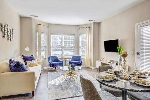 A living room with a beige couch, a blue chair, and a glass table with plates on it.