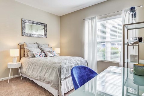 A bedroom with a bed, a chair, a nightstand, and a mirror.