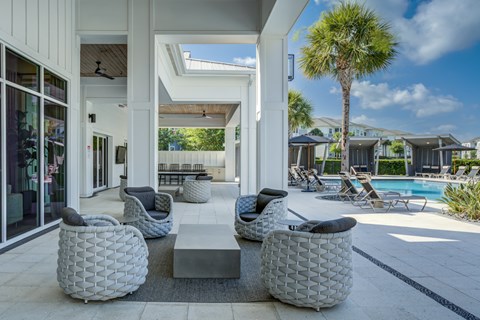 A white patio with a table and chairs and a pool in the background.