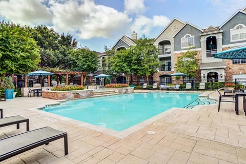 A swimming pool surrounded by a patio with chairs and umbrellas.