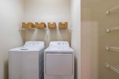 Two washing machines in a laundry room with shelves above them.