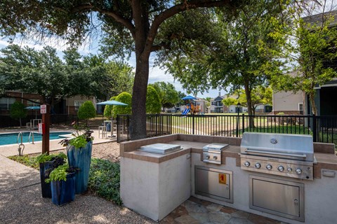 A BBQ grill is in a concrete area next to a pool.