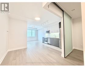 A spacious, empty room with a kitchen visible through an open door.