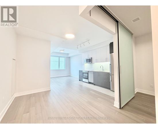 A spacious, empty room with a kitchen visible through an open door.