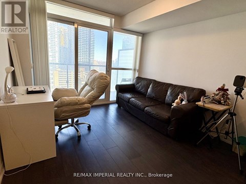 A living room with a brown couch and a chair with a computer desk in front of a window.