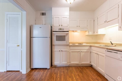 A white kitchen with wood floors and white appliances.