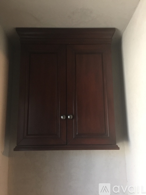 A brown cabinet with two doors and two handles is mounted on a wall.