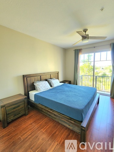 A bedroom with a bed, wooden nightstand, and a window with a view of trees.