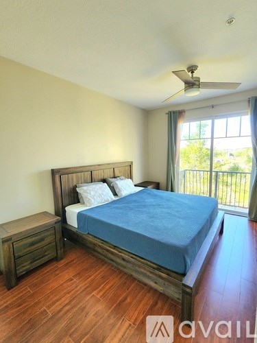A bedroom with a bed, wooden nightstand, and a window with a view of trees.