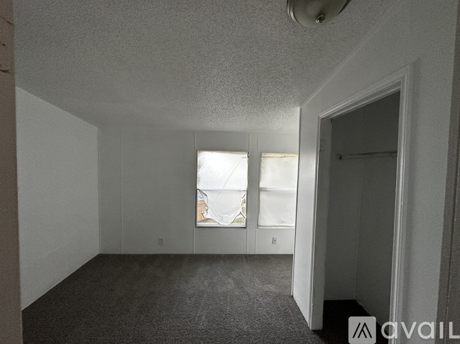 A sparsely furnished room with a carpeted floor and two windows.