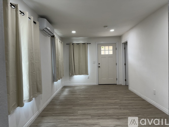 A long hallway with a door at the end and a window with curtains.