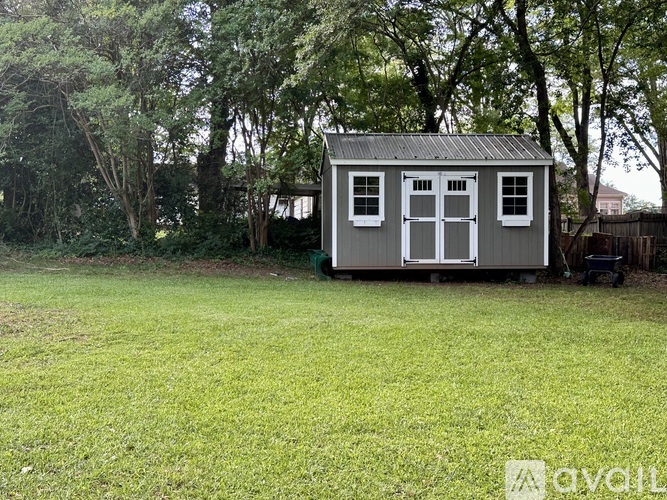A small grey shed with a metal roof is situated in a grassy area.