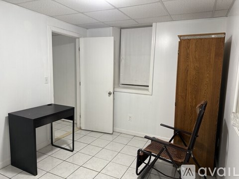 A black desk with a chair and a white fridge in the background.