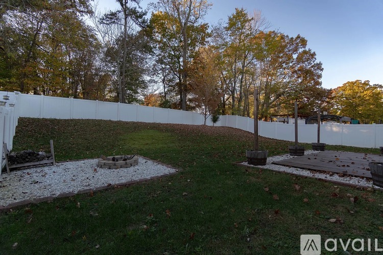 A white fence with a hedge on top divides a grassy area with a fire pit.