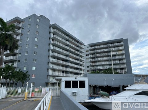 A grey apartment building with a white fence and a boat docked in front.