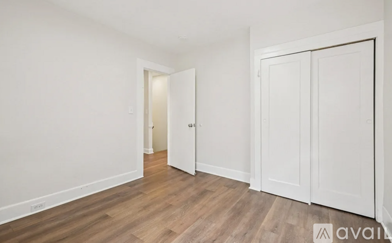 A room with white walls and wooden flooring, featuring a white door and a white wardrobe.
