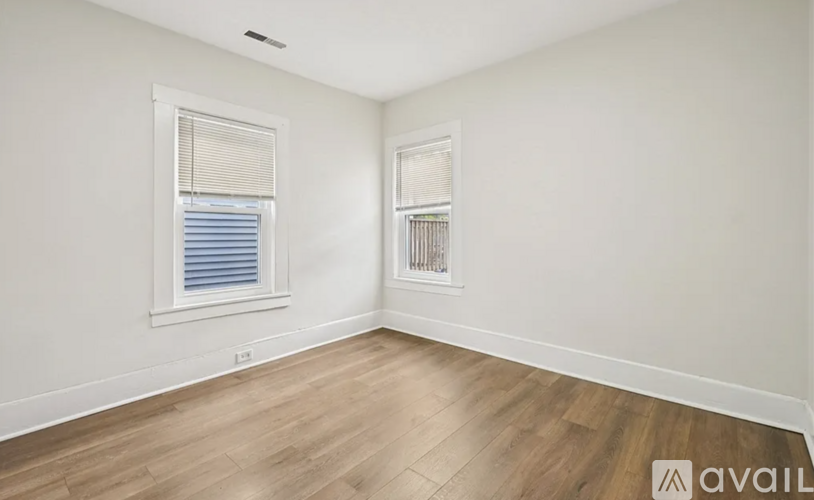 A room with wooden flooring and two windows.