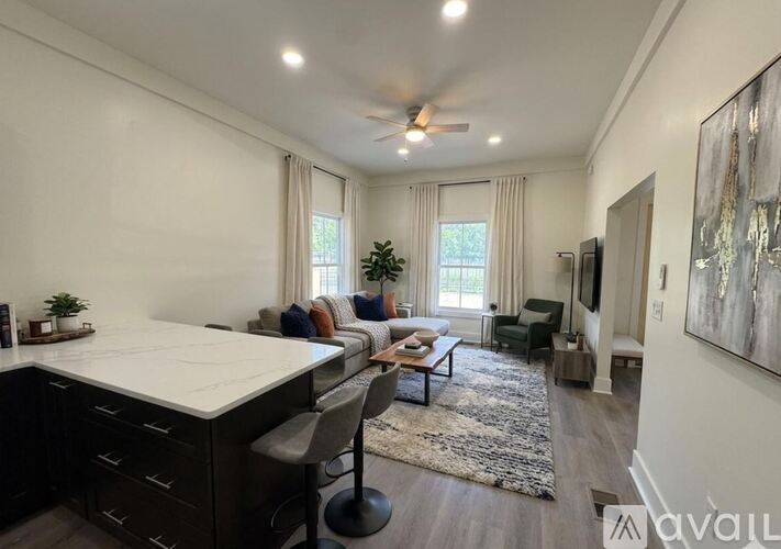 A spacious living room with a kitchen area and a ceiling fan.