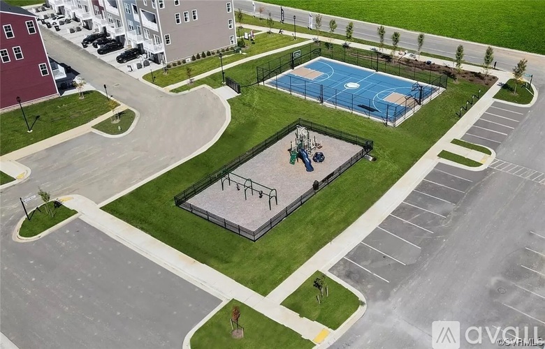 A basketball court is surrounded by a parking lot and a grassy area.