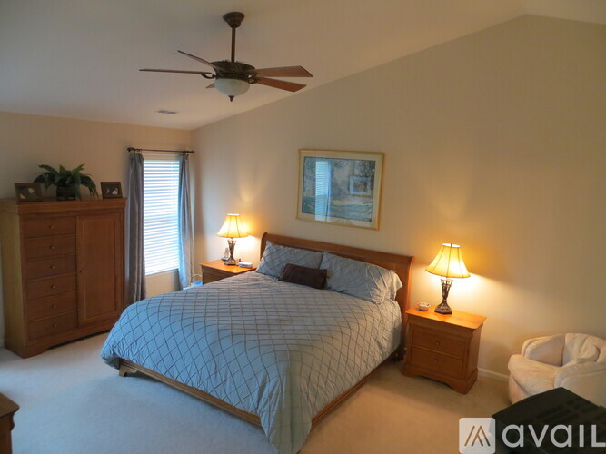 A bedroom with a bed, two lamps, a ceiling fan, and a painting on the wall.