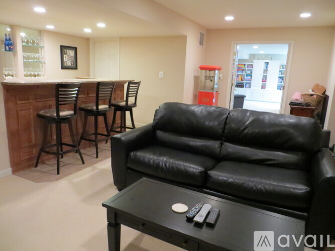 A black leather couch sits in a living room with a bar area in the background.