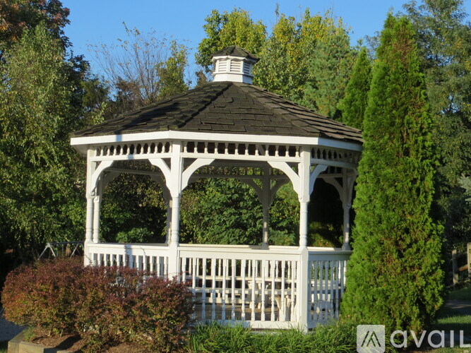 A white gazebo with a black roof is surrounded by greenery.