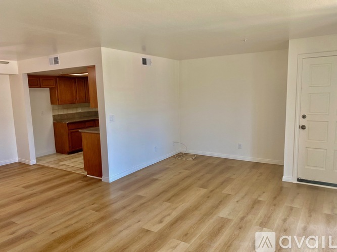 A room with wooden flooring and white walls, with a door on the right and a cabinet with a countertop in the background.