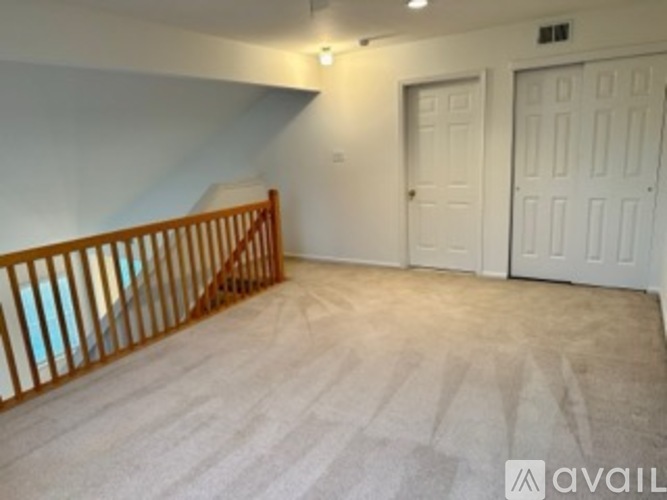 A room with a carpeted floor, a staircase with wooden railings, and two doors.