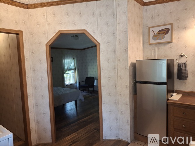 A kitchen with a refrigerator, a mirror, and a bedroom with a bed and a window.