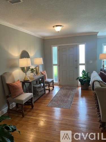 A living room with a chair, a table with a lamp and a mirror, and a rug on the floor.