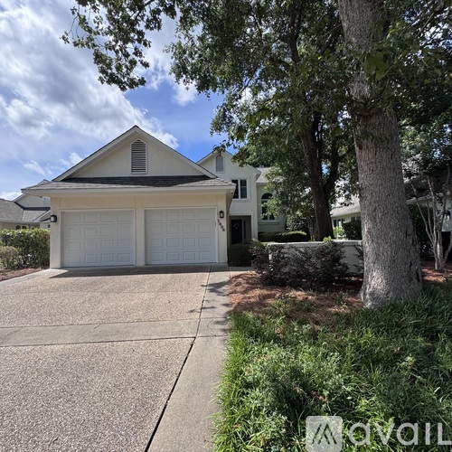 A house with a white garage door is surrounded by greenery.