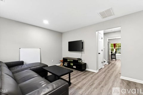 A black leather couch sits in a living room with a television and a whiteboard on the wall.