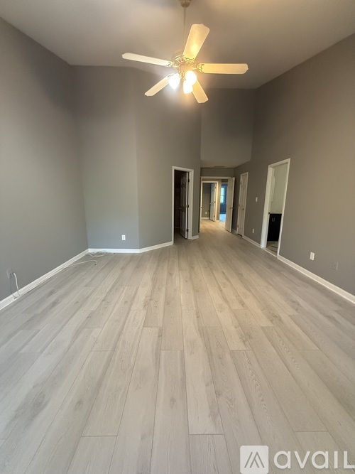 A spacious room with a ceiling fan and light, and wooden flooring.
