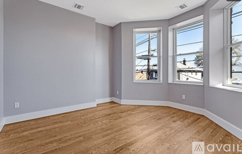 A room with wooden flooring and three windows.