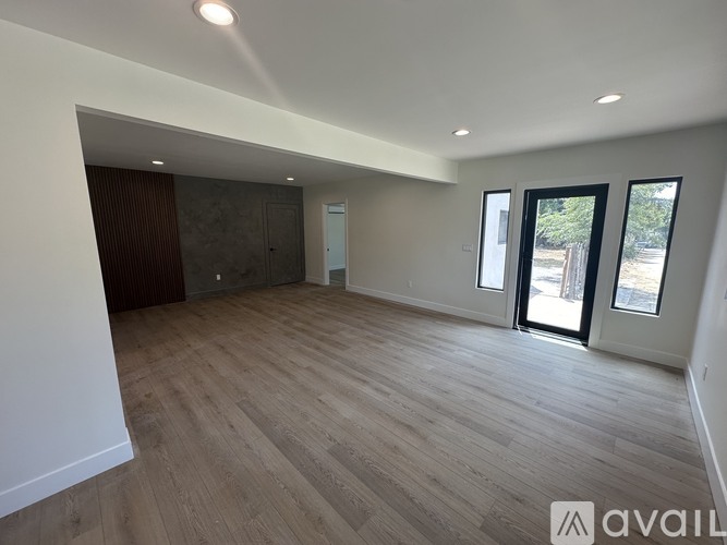A spacious room with wooden flooring and a sliding glass door.