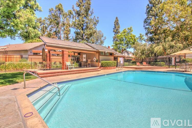 A swimming pool in front of a house with a fence and trees in the background.