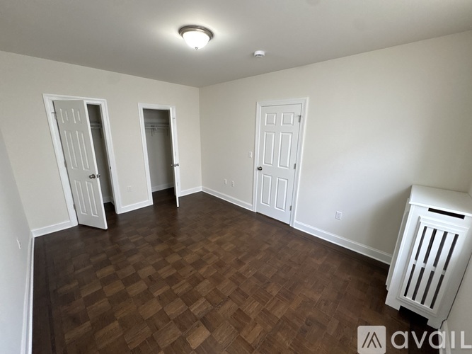 A room with wooden flooring and white walls with three doors.