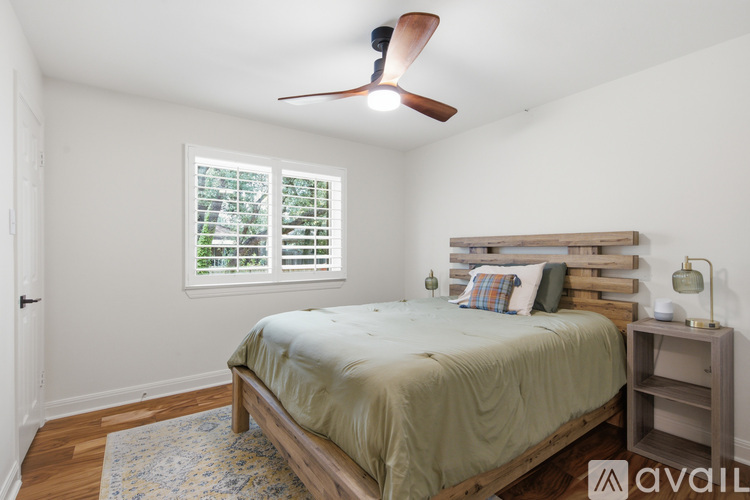 A bedroom with a bed, a fan, and a window with blinds.