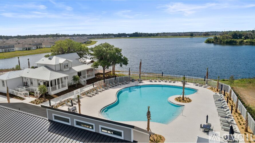 A large swimming pool is surrounded by a white fence and a house with a white roof is in the background.